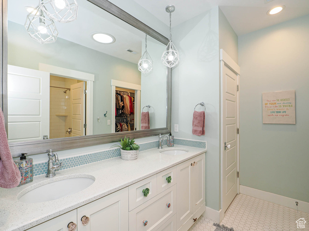 Bathroom featuring double vanity, a shower, a walk in closet, baseboards, and tile patterned floors
