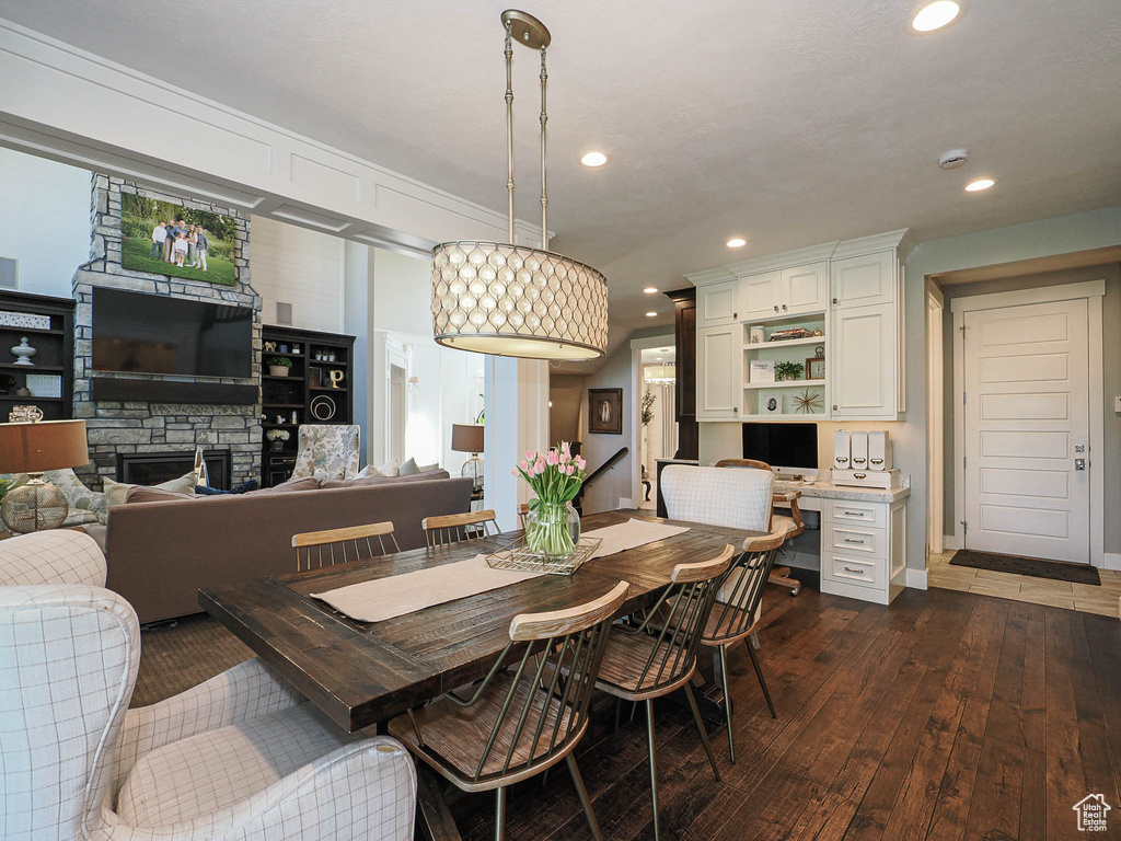 Dining area with dark wood-type flooring, recessed lighting, a stone fireplace, and baseboards