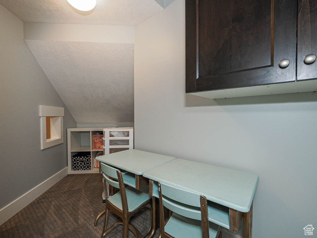 Dining room featuring a textured ceiling, dark carpet, baseboards, and lofted ceiling
