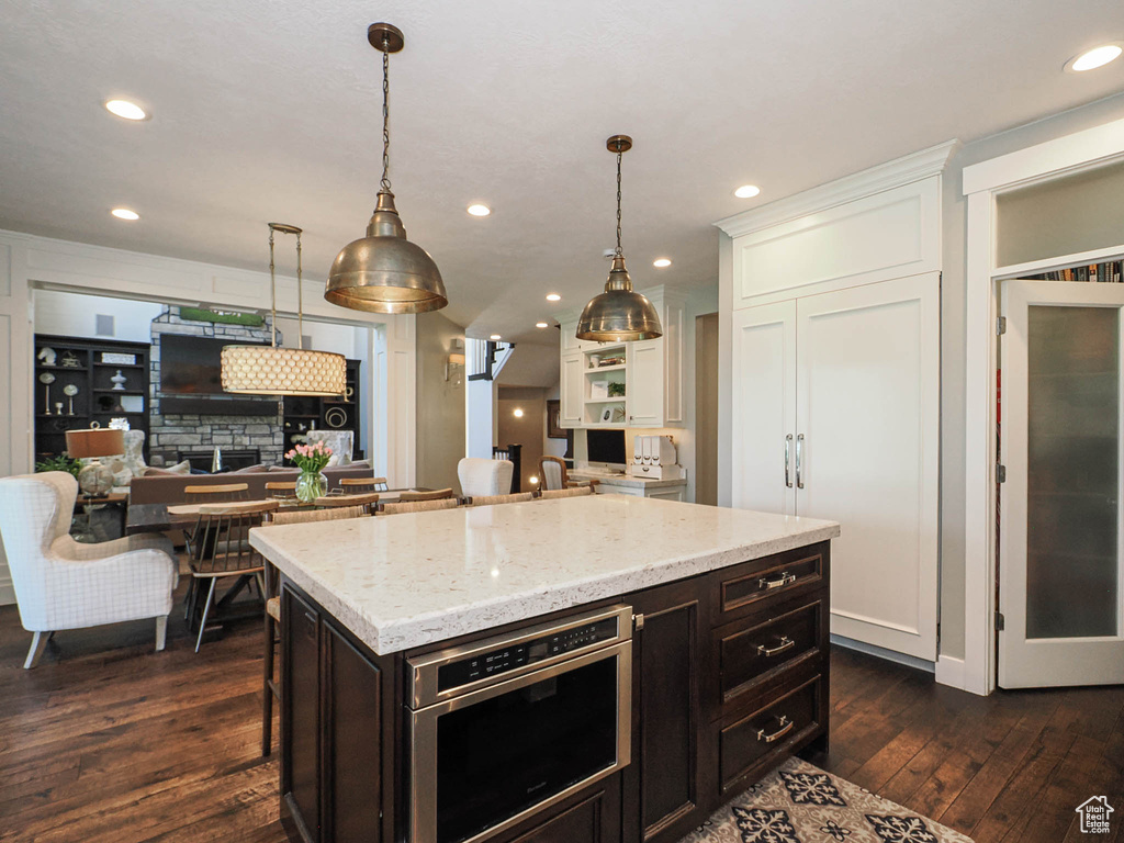 Kitchen featuring dark wood-style floors, light stone counters, decorative light fixtures, white cabinetry, and recessed lighting