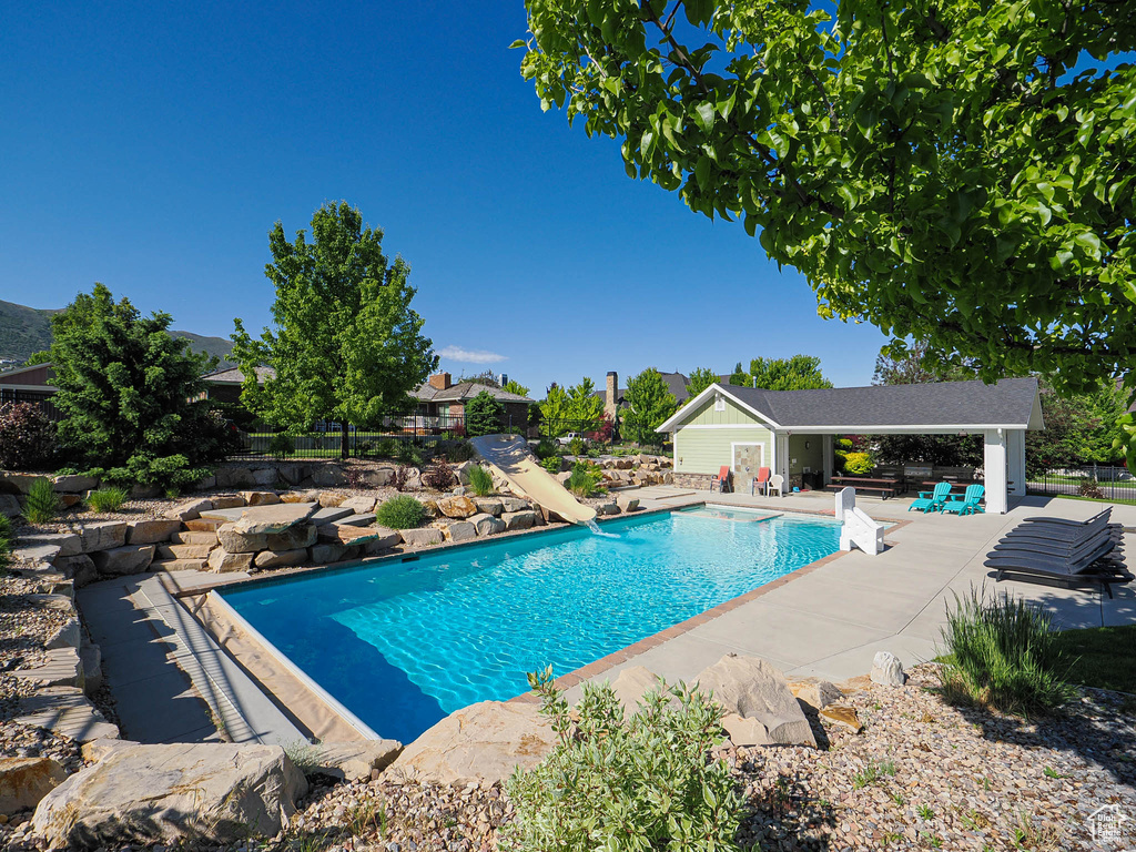 Outdoor pool with a patio, a storage structure, an outbuilding, and a water slide