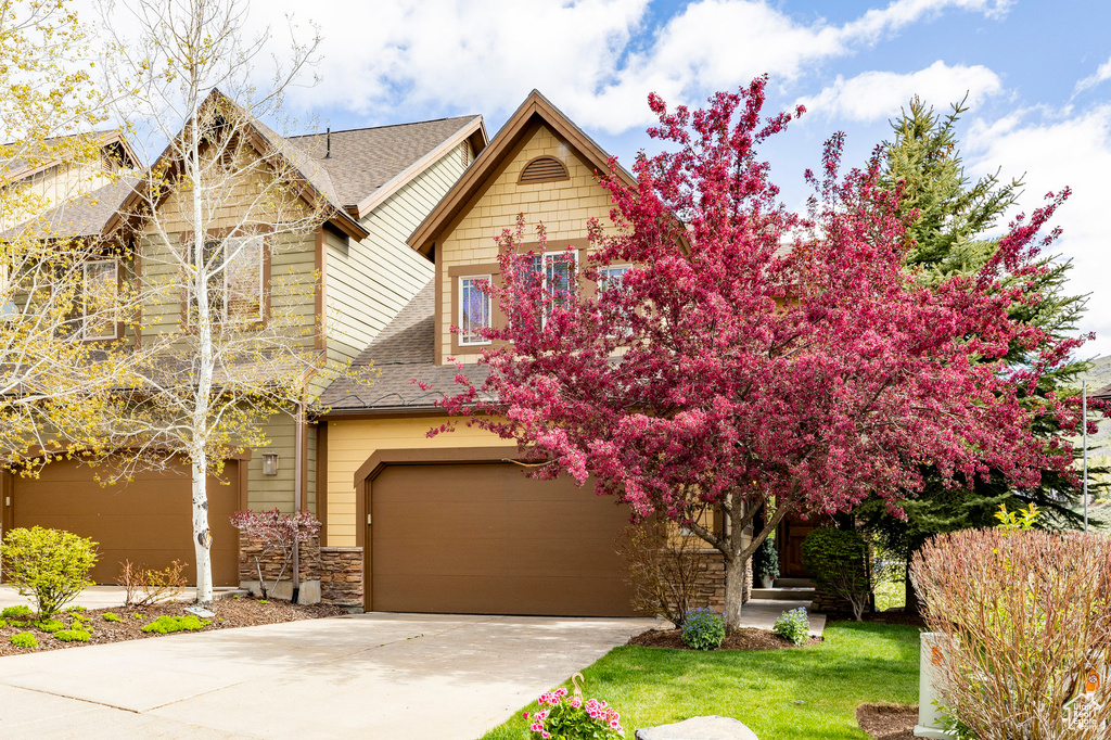 View of front of home featuring a garage, roof with shingles, driveway, and stone siding