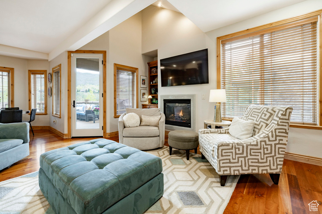 Living area featuring baseboards, hardwood / wood-style flooring, vaulted ceiling, a glass covered fireplace, and healthy amount of natural light