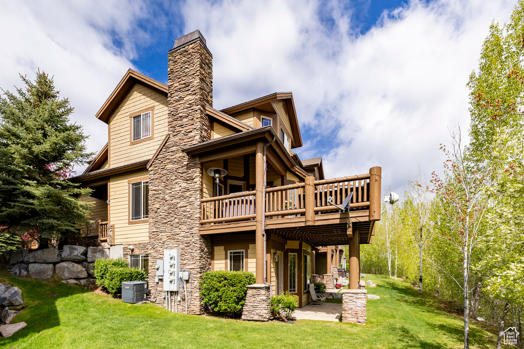 Rear view of property featuring central AC, a yard, a chimney, stone siding, and a patio area