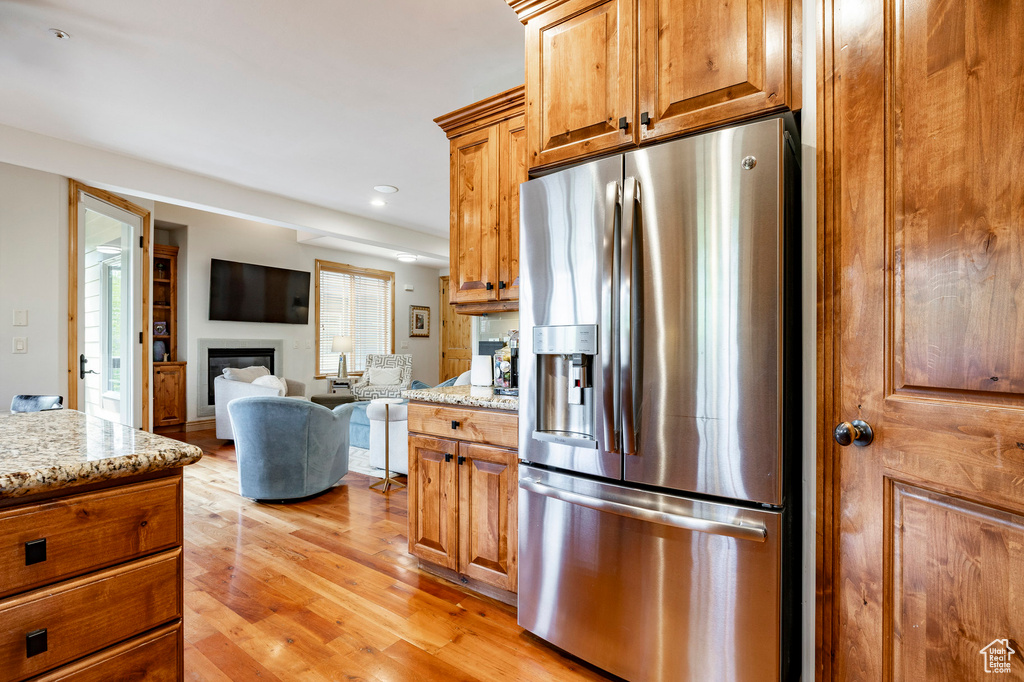 Kitchen featuring stainless steel refrigerator with ice dispenser, a glass covered fireplace, light wood-type flooring, light stone countertops, and recessed lighting