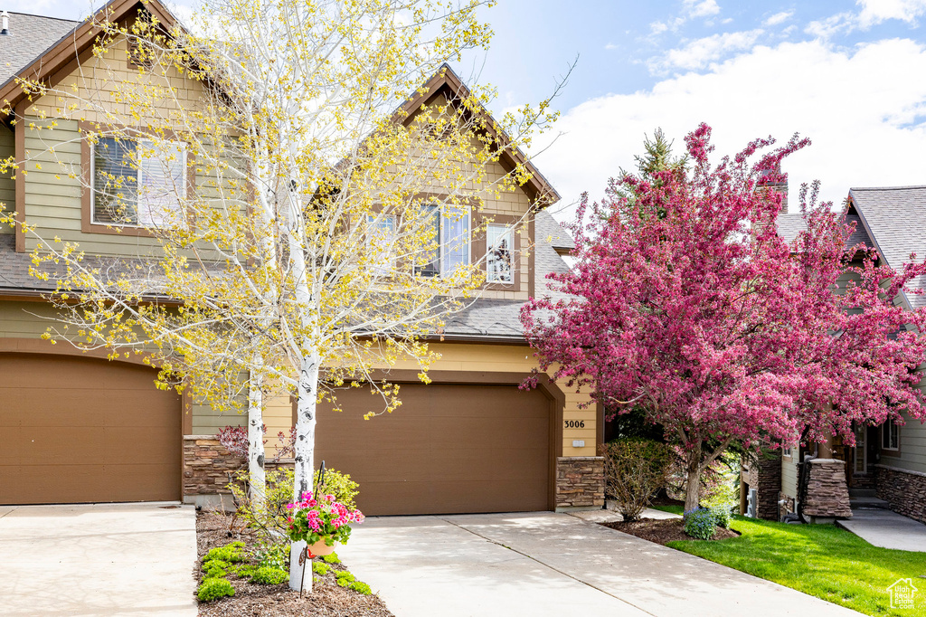 Craftsman-style home featuring a garage, roof with shingles, concrete driveway, and stone siding