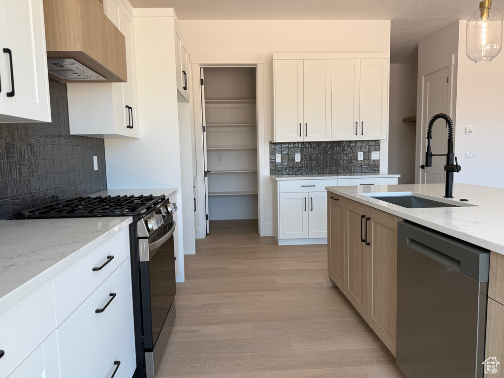 Kitchen featuring stainless steel appliances, wall chimney range hood, light stone counters, backsplash, and light wood finished floors