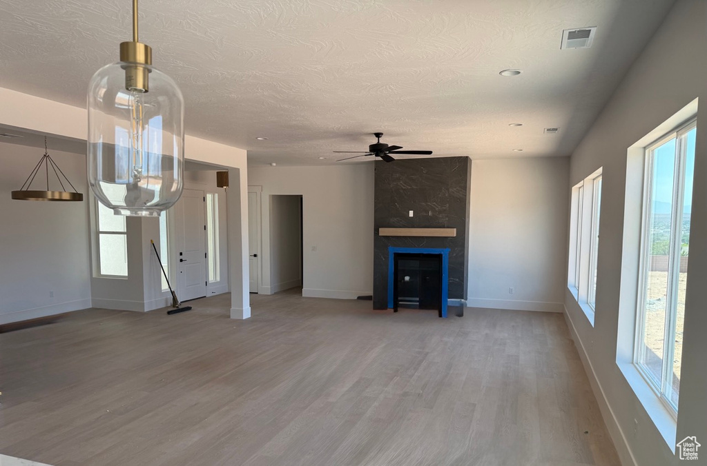 Unfurnished living room with light wood-style floors, ceiling fan, a textured ceiling, and a large fireplace