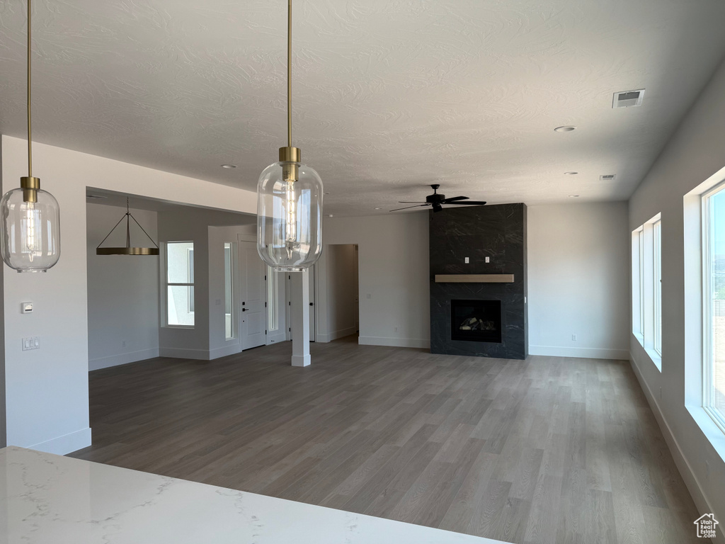 Unfurnished living room featuring wood finished floors, ceiling fan, healthy amount of natural light, a fireplace, and a textured ceiling