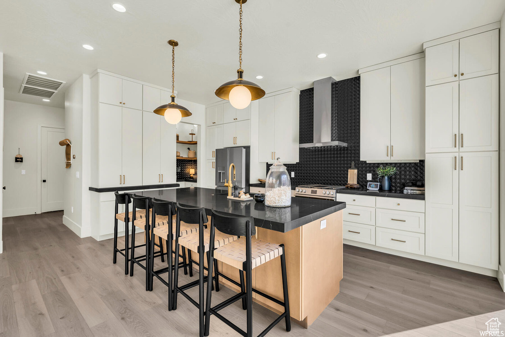 Kitchen with wall chimney exhaust hood, dark countertops, light wood finished floors, a kitchen breakfast bar, and recessed lighting