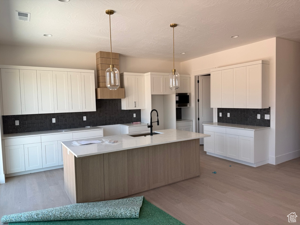 Kitchen with light wood-type flooring, decorative backsplash, a center island with sink, white cabinets, and recessed lighting