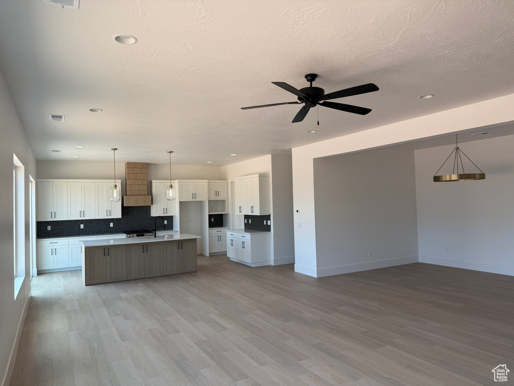 Kitchen with open floor plan, premium range hood, white cabinetry, light wood finished floors, and recessed lighting