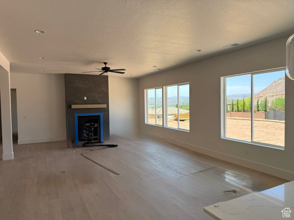 Unfurnished living room with a ceiling fan, wood finished floors, a large fireplace, a textured ceiling, and recessed lighting
