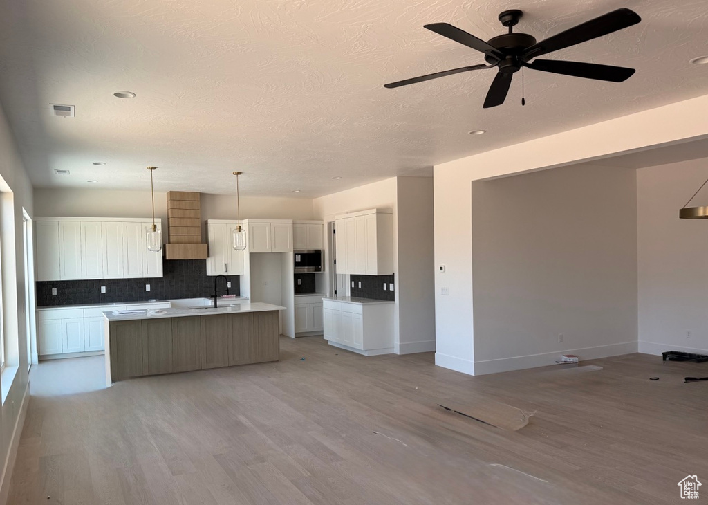 Kitchen featuring stainless steel microwave, backsplash, a center island with sink, open floor plan, and recessed lighting