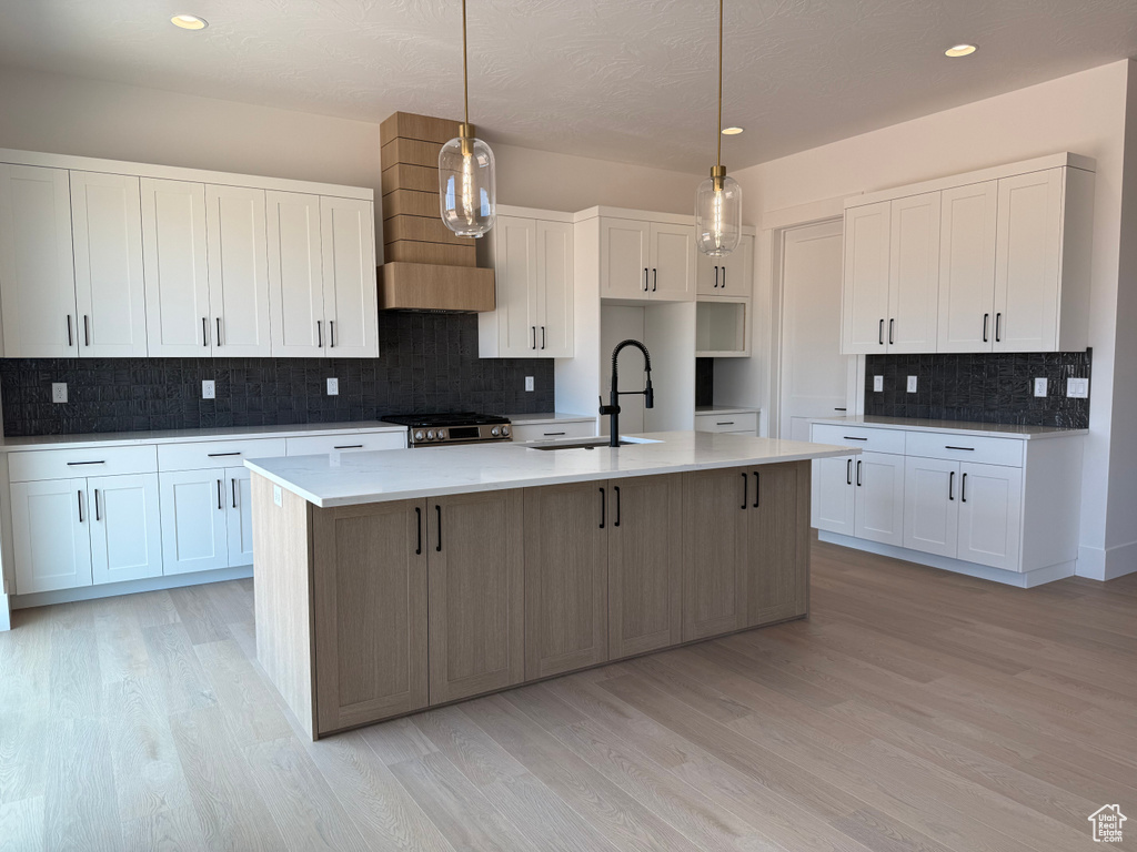 Kitchen with tasteful backsplash, a kitchen island with sink, light wood-style flooring, white cabinetry, and recessed lighting