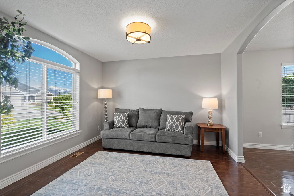 Living area featuring arched walkways, healthy amount of natural light, baseboards, and a textured ceiling