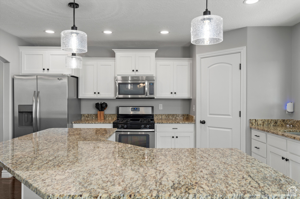 Kitchen featuring stainless steel appliances, a kitchen island, white cabinetry, recessed lighting, and light stone counters
