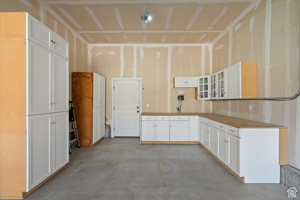 Kitchen featuring concrete floors, glass insert cabinets, and white cabinetry