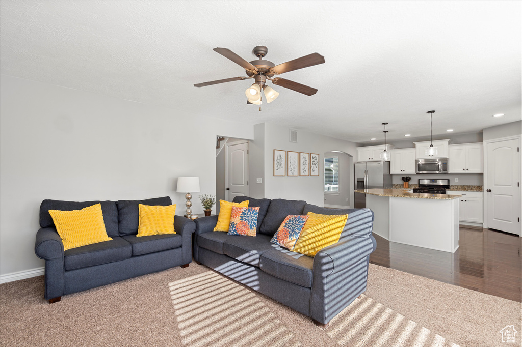 Living area featuring ceiling fan, recessed lighting, arched walkways, dark carpet, and baseboards