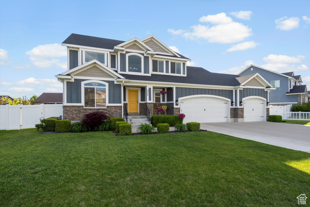Craftsman-style house with stone siding, a garage, board and batten siding, driveway, and roof with shingles