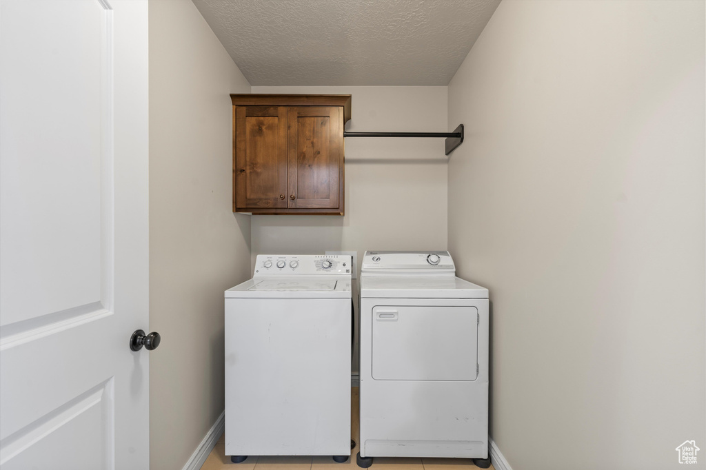 Laundry room featuring washer and clothes dryer, cabinet space, a textured ceiling, baseboards, and light tile patterned floors