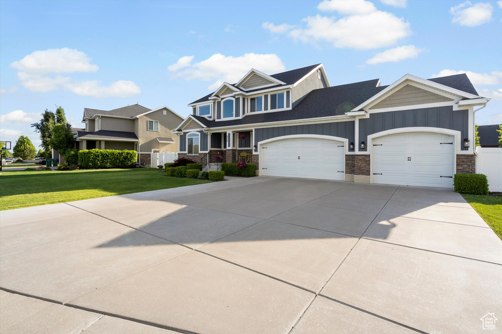 View of front of home with stone siding, board and batten siding, a garage, and a front lawn