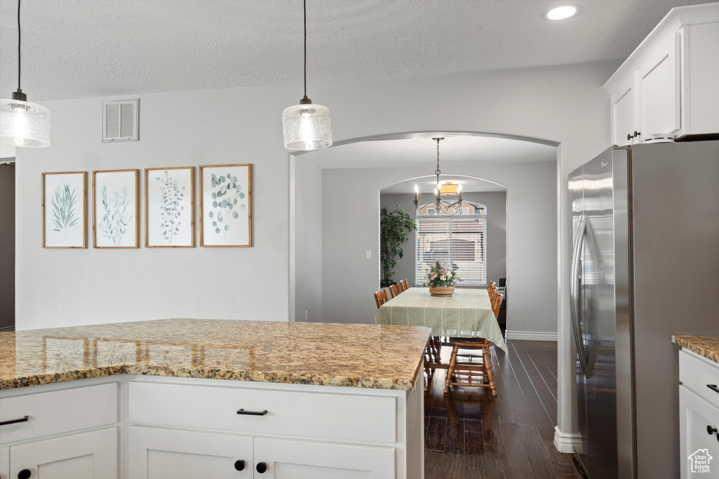 Kitchen featuring freestanding refrigerator, arched walkways, white cabinets, light stone counters, and dark wood-type flooring