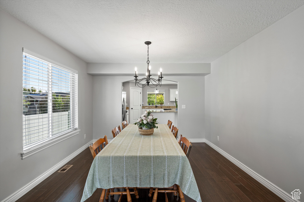 Dining room with a chandelier, dark wood-type flooring, baseboards, and a textured ceiling