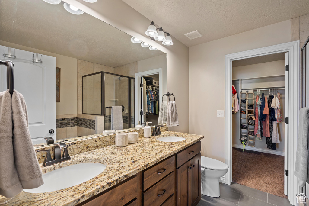 Bathroom featuring a walk in closet, double vanity, a stall shower, toilet, and a textured ceiling