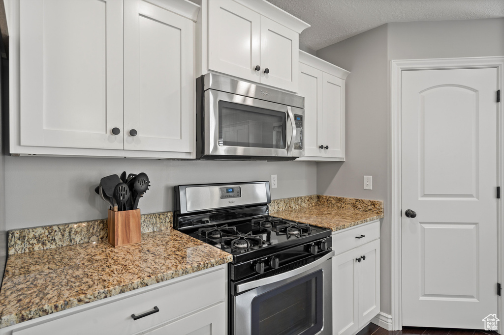 Kitchen with appliances with stainless steel finishes, light stone countertops, white cabinetry, and a textured ceiling