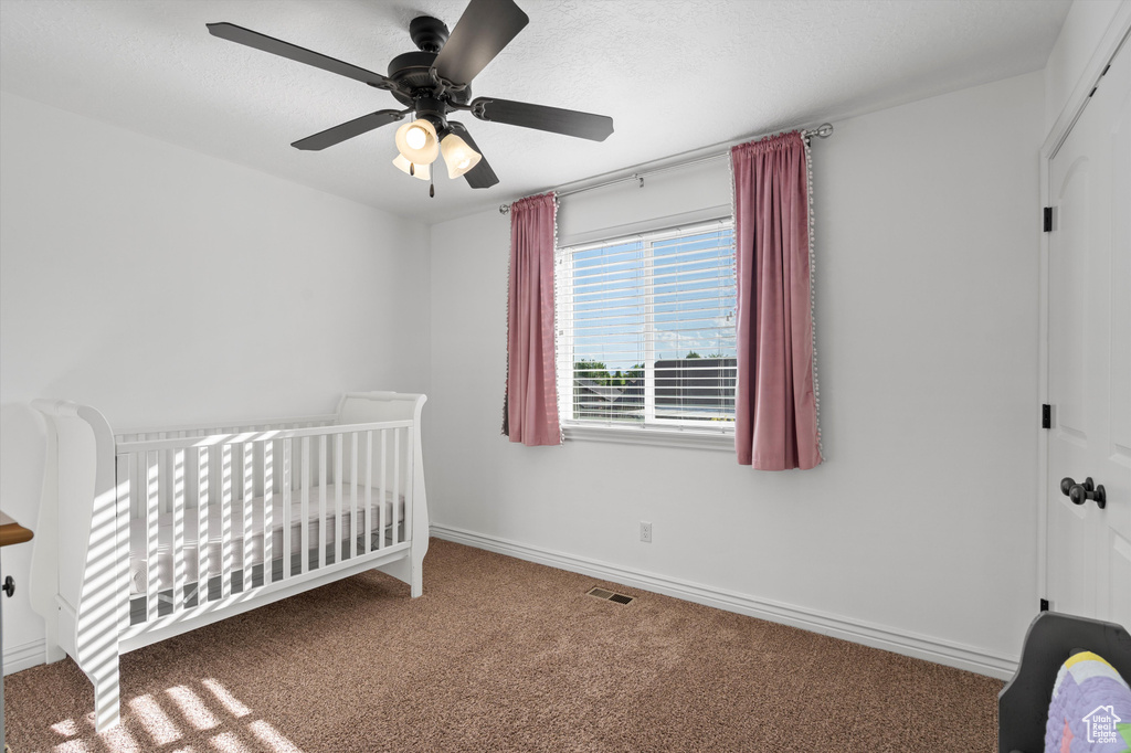 Carpeted bedroom featuring a nursery area, baseboards, and ceiling fan