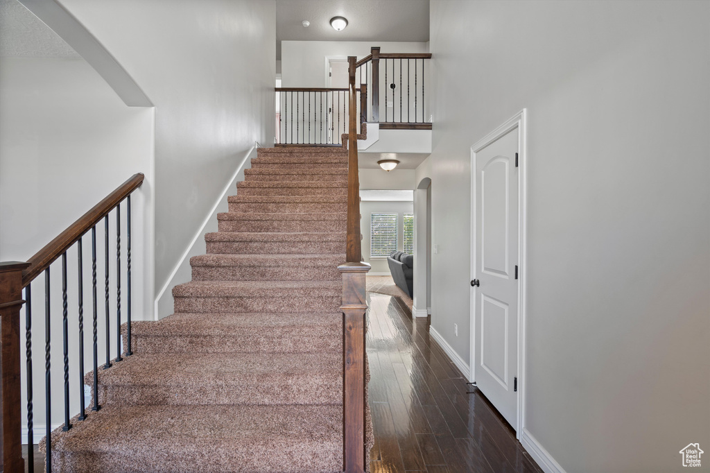 Stairs with arched walkways, baseboards, wood finished floors, and a high ceiling