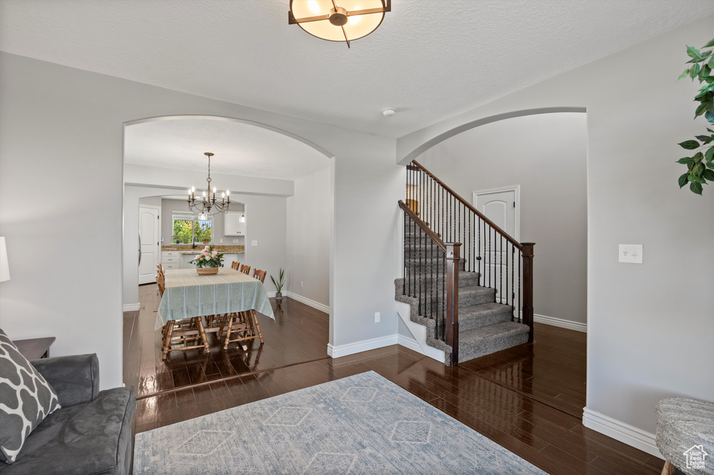 Foyer entrance with arched walkways, wood finished floors, stairs, baseboards, and a chandelier