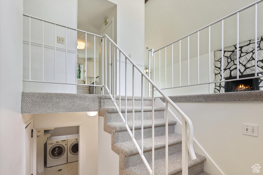 Stairs with washing machine and clothes dryer, a stone fireplace, and a towering ceiling