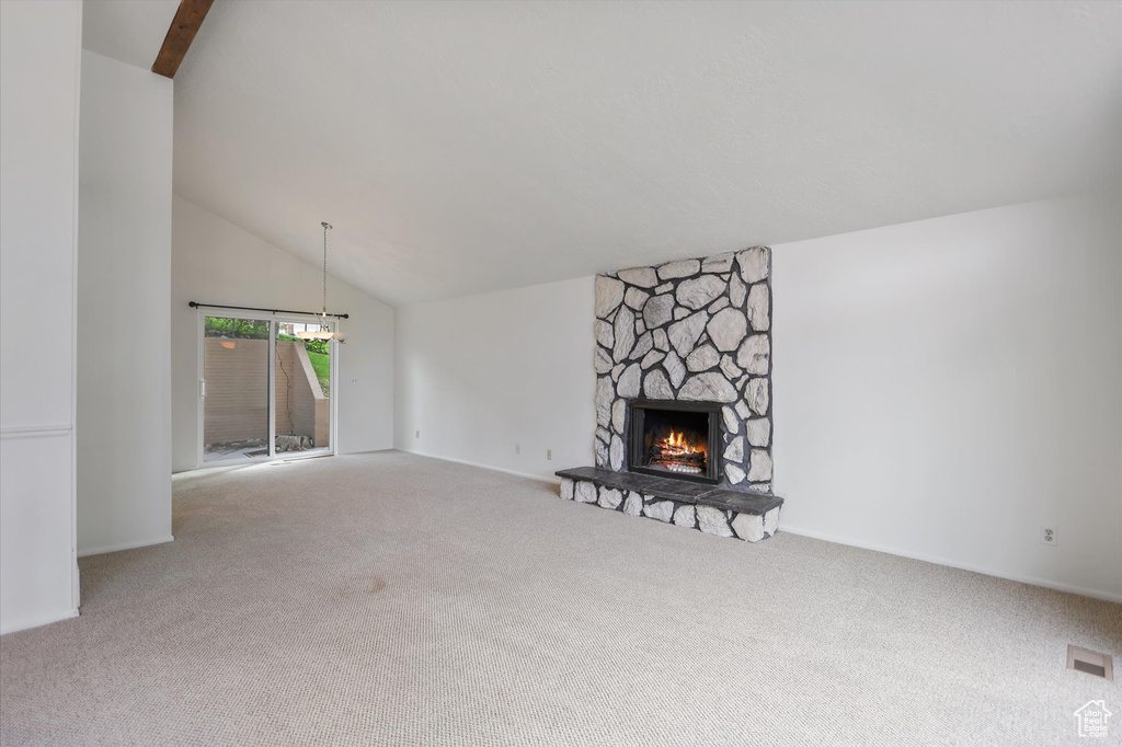 Unfurnished living room with carpet flooring, vaulted ceiling, a stone fireplace, and a chandelier