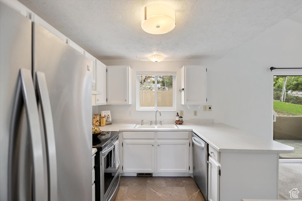 Kitchen featuring stainless steel appliances, a sink, a peninsula, a textured ceiling, and white cabinets