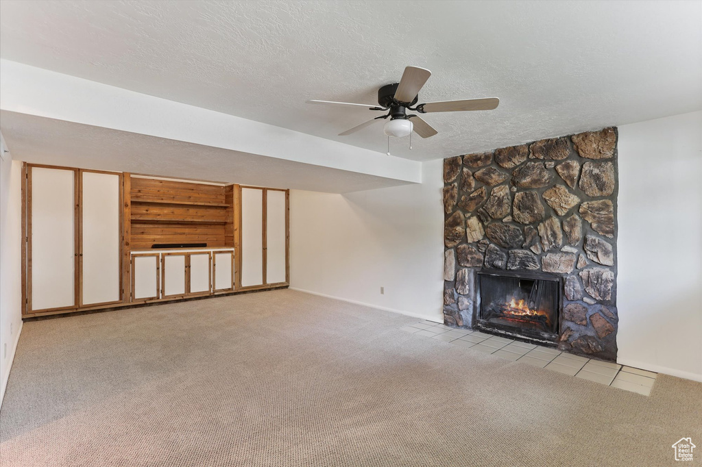 Unfurnished living room with carpet floors, a textured ceiling, a stone fireplace, baseboards, and ceiling fan