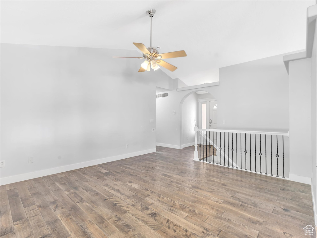 Unfurnished room with arched walkways, a ceiling fan, vaulted ceiling, wood finished floors, and baseboards