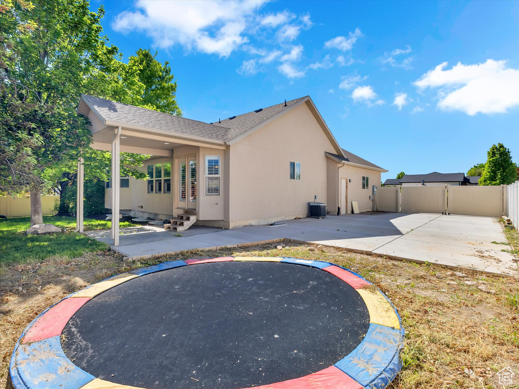 Rear view of house with a patio, a fenced backyard, a trampoline, stucco siding, and entry steps