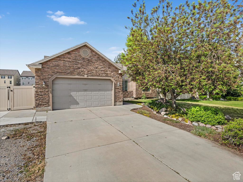 View of front of house with an attached garage, driveway, stone siding, and a gate