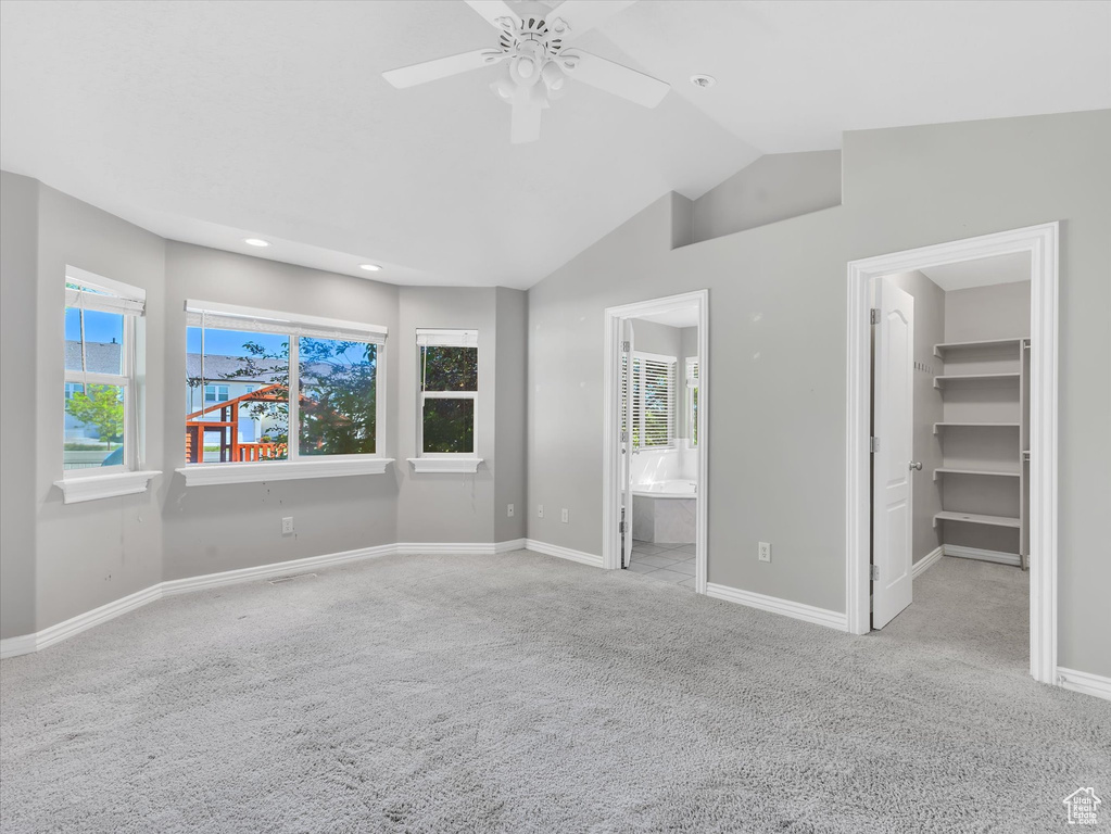 Unfurnished bedroom featuring carpet floors, a spacious closet, baseboards, lofted ceiling, and ensuite bath