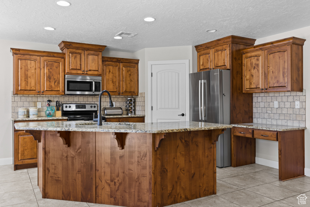 Kitchen featuring stainless steel appliances, light stone countertops, backsplash, recessed lighting, and a textured ceiling