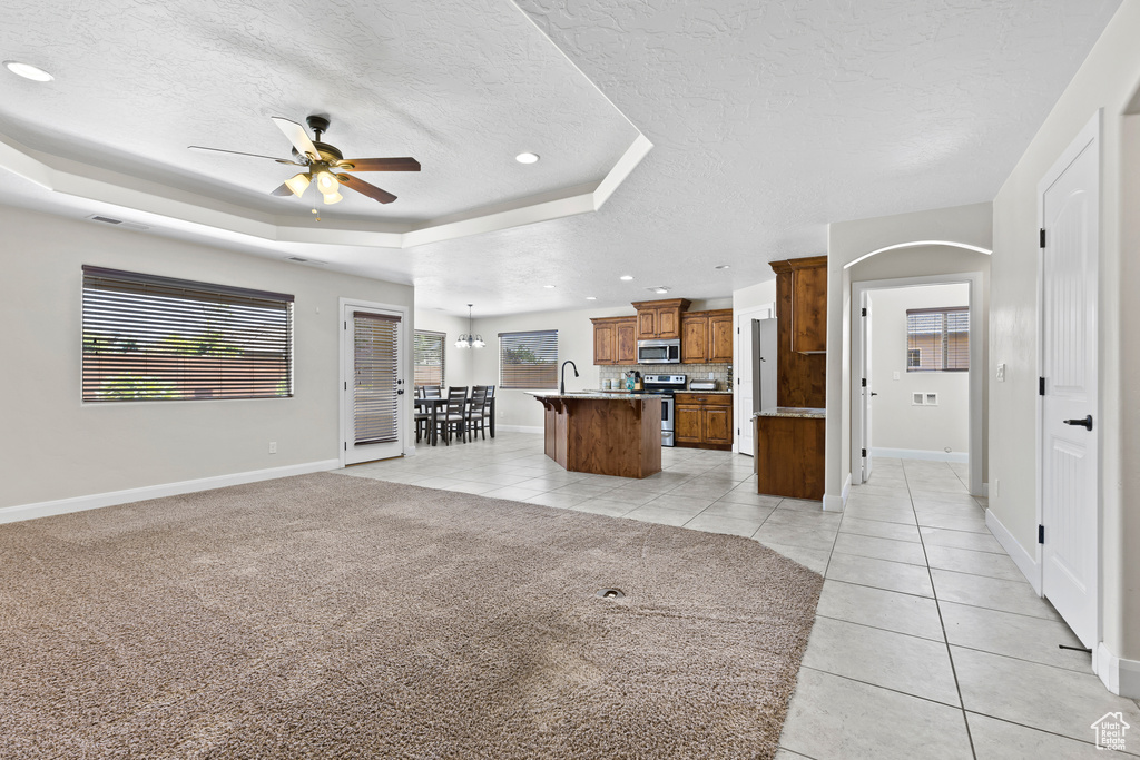 Unfurnished living room with a ceiling fan, light tile patterned floors, a textured ceiling, a raised ceiling, and baseboards