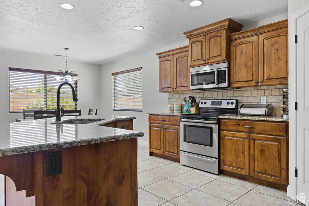 Kitchen with appliances with stainless steel finishes, a sink, tasteful backsplash, a chandelier, and pendant lighting