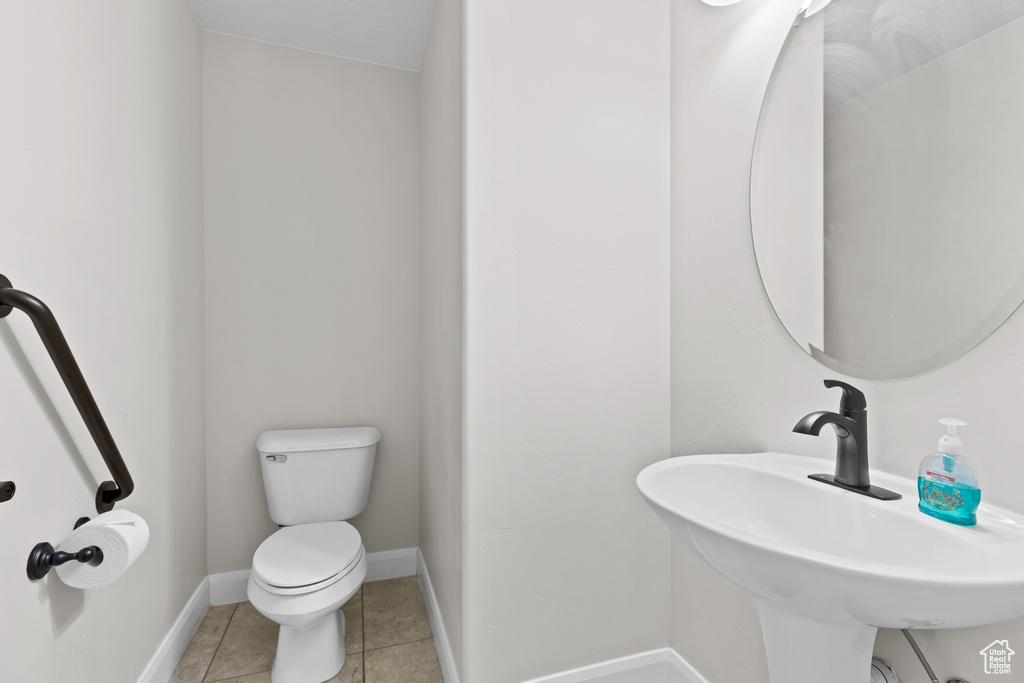 Half bathroom with toilet, a sink, baseboards, and tile patterned floors