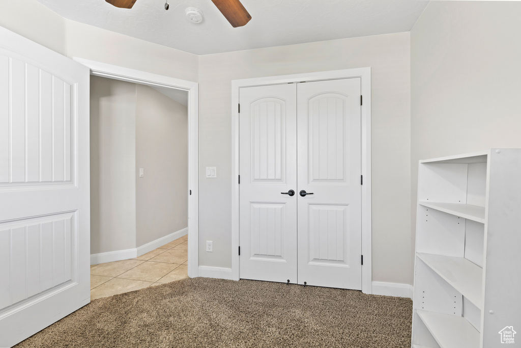 Unfurnished bedroom featuring light carpet, a closet, baseboards, a ceiling fan, and light tile patterned floors
