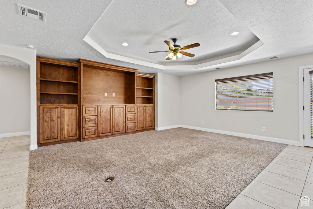 Unfurnished living room featuring a tray ceiling, a textured ceiling, a ceiling fan, baseboards, and light tile patterned flooring