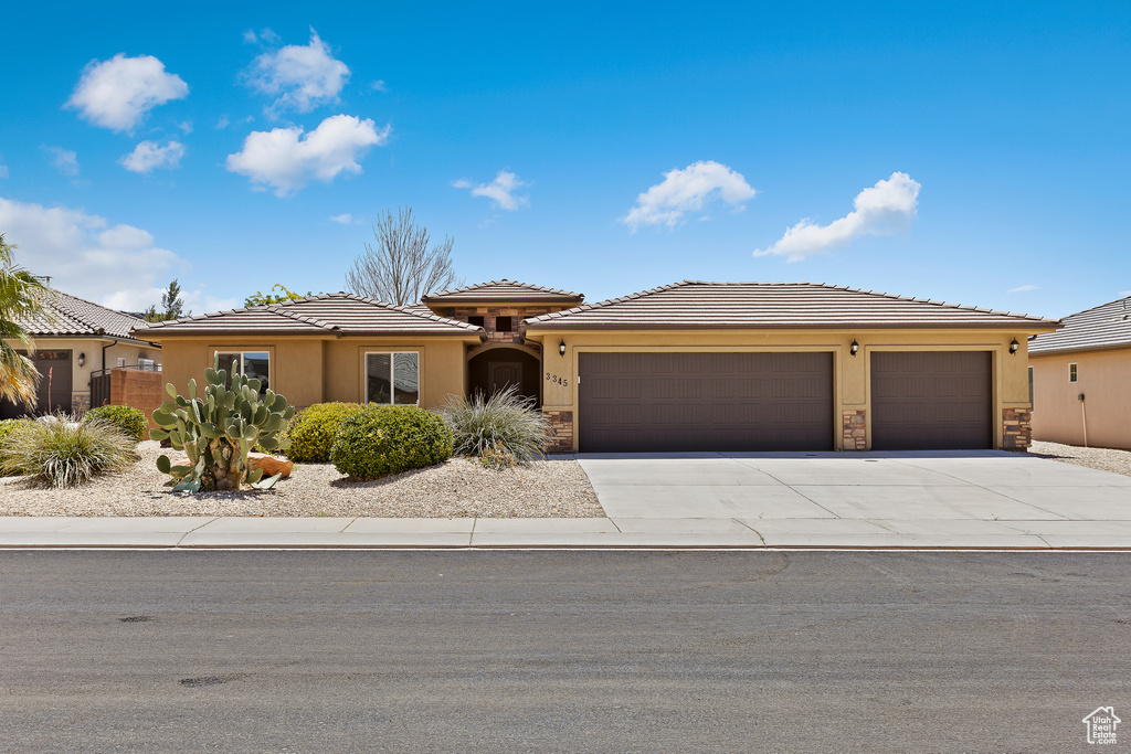 Prairie-style home featuring a garage, stone siding, driveway, and stucco siding