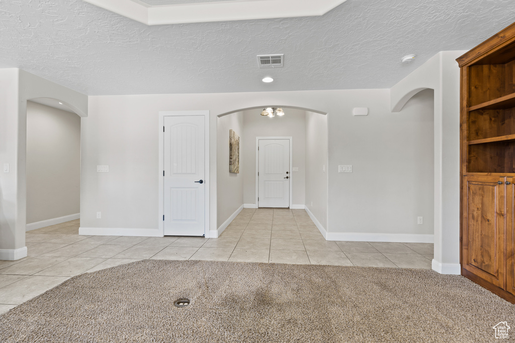 Foyer entrance with arched walkways, light tile patterned floors, a textured ceiling, baseboards, and light colored carpet