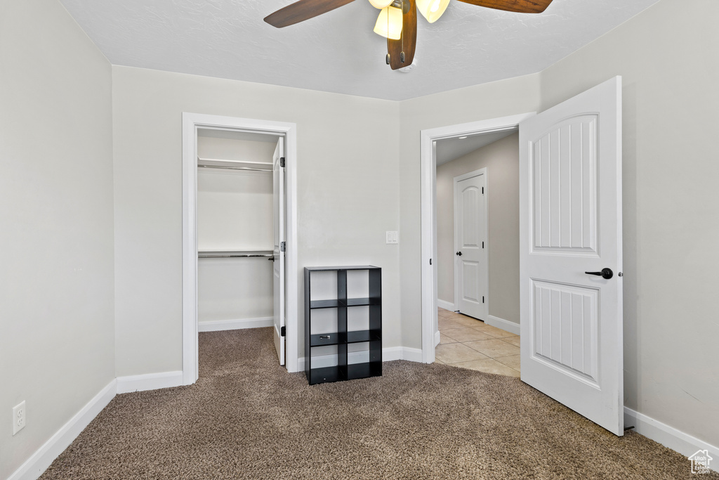 Unfurnished bedroom with carpet flooring, a spacious closet, a closet, a ceiling fan, and baseboards